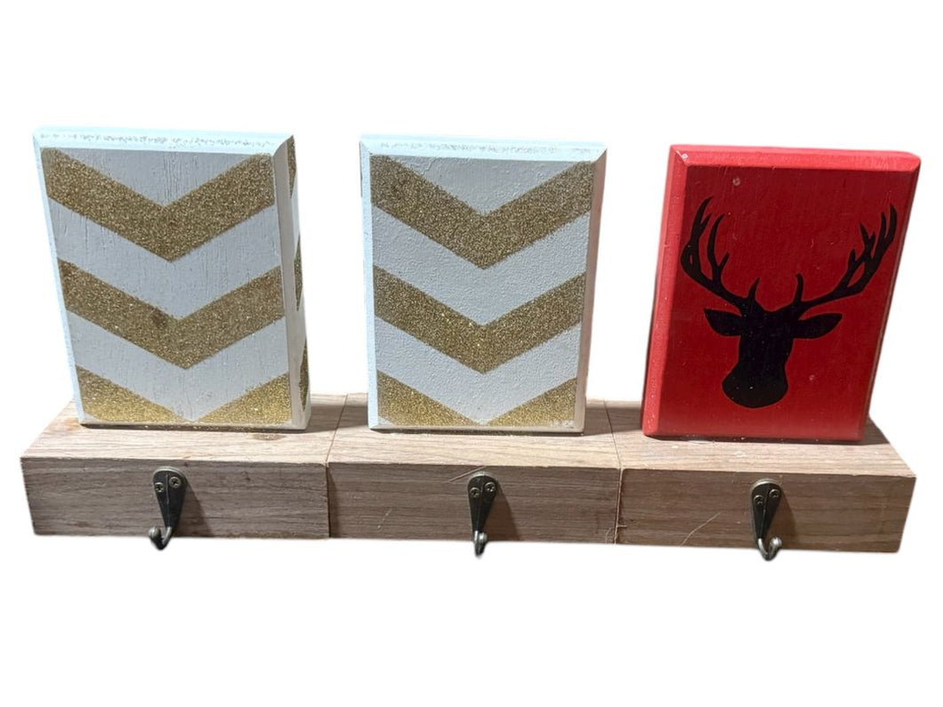 3 wooden stocking holders 2 white and gold, 1 red with a deer